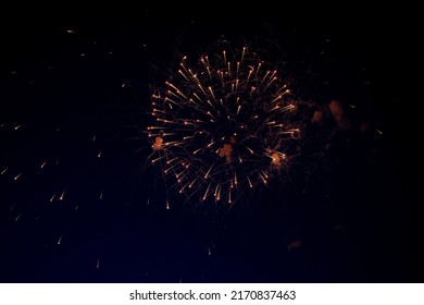 A bright ball of fireworks with orange sparks and a lot of sparks around on the background of the night sky. High quality photo