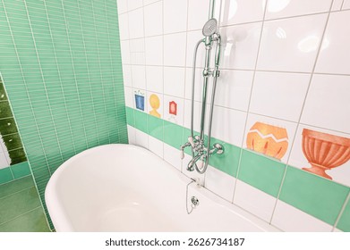 bright bathroom with mint green and white tiles. Features a pink ceiling and a chrome shower fixture. Child-like drawings decorate the tiles.