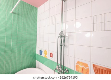 bright bathroom with mint green and white tiles. Features a pink ceiling and a chrome shower fixture. Child-like drawings decorate the tiles.