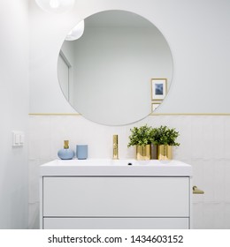 Bright Bathroom With Round Mirror, White Cabinet With Drawers And Blue And Golden Decorations