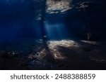 A bright beam of sunlight shines underwater illuminating a shallow sandy seafloor in Alor, Indonesia. 