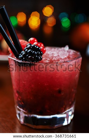 bright beautiful and tasty cocktail or lemonade with a cap of frozen ice and fresh berries on the bar with a nice bokeh of the disco light. soft focus.