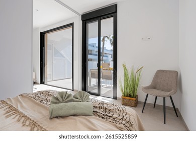 Bright bedroom featuring a patterned bedspread, sliding doors to a private patio, and minimal decor with a chair and potted plant.