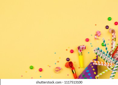 Bright Birthday Party Background With Cocktail Tubes, Hat, Horn And Candy. Multicolored Holiday Accessories On Yellow Table. Copy Space, Top View