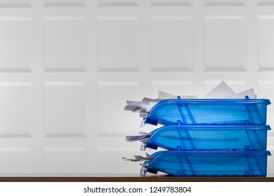 Bright blue filing trays overflowing with paperwork, receipts, accounts with a white contemporary panelled wall background. 