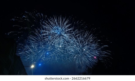 Bright blue fireworks exploding in the dark night sky, lighting up the atmosphere with sparkling blue hues and vibrant bursts of light