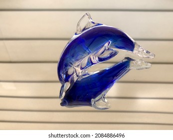 Bright blue glass dolphin figurine sitting on a mirror with its reflection - Shutterstock ID 2084886496