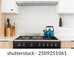 Bright blue kettle on a gas stove, black free standing oven, vertical textured wall tile, white top cabinets, pull out extractor fan, styled white counter tops