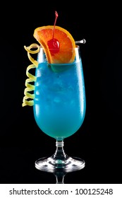Bright Blue Lagoon cocktail over black background on reflection surface, garnished with orange slice, maraschino cherry, and lemon twist. Most popular cocktails series