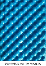 The bright blue mat has a bumpy, textured surface. The small circles are organized in a grid pattern. Deep shadows and bright highlights create a sense of depth.


