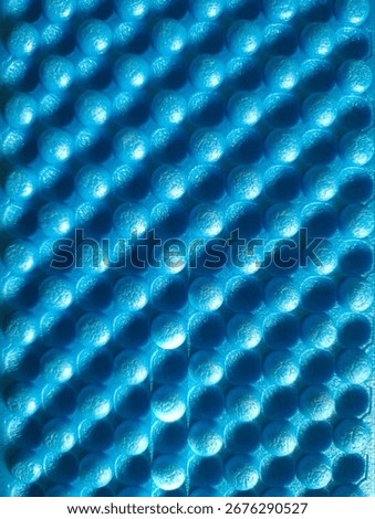 The bright blue mat has a bumpy, textured surface. The small circles are organized in a grid pattern. Deep shadows and bright highlights create a sense of depth.

