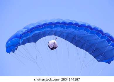 Bright blue parachute fully deployed, seen from below against clear sky
