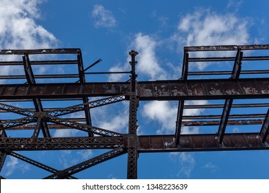 Bright Blue Sky Cut Through By Elevated Rotting Steel Train Tracks With Light Cloud Cover