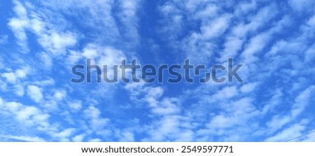 A bright blue sky with a dynamic pattern of white clouds, creating a serene and beautiful background. Ideal for nature themes or creative project backgrounds.