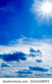 Bright blue sky filled with dramatic, fluffy white clouds. Sunbeams pierce through the clouds, creating a stunning, radiant, and peaceful natural scene.
