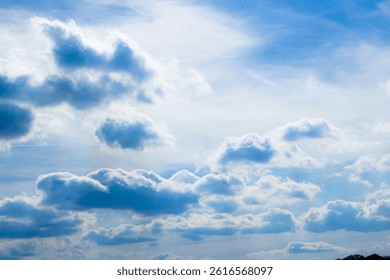 Bright blue sky filled with dramatic, fluffy white clouds. Sunbeams pierce through the clouds, creating a stunning, radiant, and peaceful natural scene.