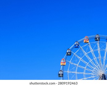 Bright blue sky frames a towering Ferris wheel. Colorful gondolas hang in silent suspension. Cable structure glows against crisp atmosphere. No people, no motion-quiet, serene, still moment.