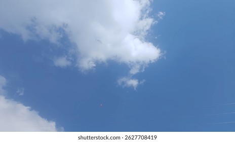 bright blue sky with some fluffy white clouds. In the bottom center of the image, a small red balloon is visible.