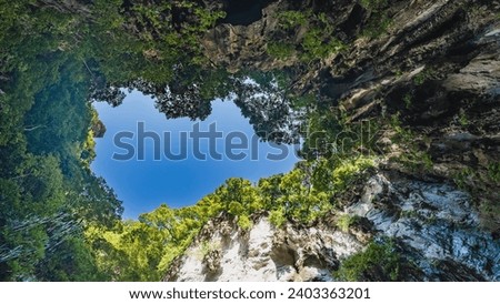 The bright blue sky is visible through the hole in the roof of the cave. Thickets of green trees on steep rocky slopes. Batu caves. Malaysia. Kuala Lumpur