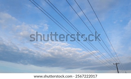 
A bright blue sky with wispy clouds, cut by stripes of stretched power lines. Displays a calm and slightly melancholic atmosphere.