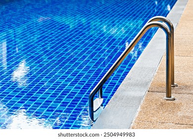 Bright blue tiled swimming pool with stainless steel ladder, leading into water, creating refreshing and inviting atmosphere - Powered by Shutterstock