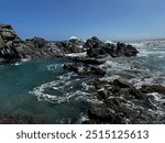 Bright blue water crashing on blackened rocks with a small natural pond attached.