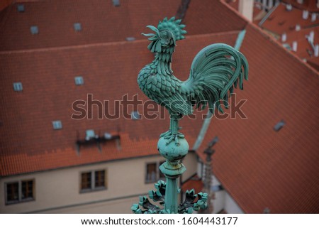 Bright blue-greenish rooster. Crowing copper symbol of St. Vitus. Gothic cathedral roof tiles structure & patterns. St. Vitus verdigris patina cock on the crest of the roof. Old chimneys & red roofs.