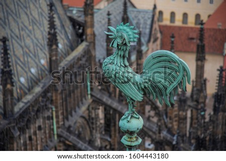 Bright blue-greenish rooster. Crowing copper symbol of St. Vitus. Gothic cathedral spires. Roof tiles structure and grey-black symmetric patterns. St. Vitus verdigris patina cock on roof crest. 