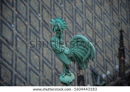 Bright blue-greenish rooster. Crowing copper symbol of St. Vitus. Gothic cathedral roof tiles structure and grey-black symmetric patterns. St. Vitus verdigris patina cock on the crest of the roof.