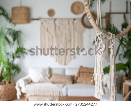 A bright bohemian interior features macrame wall art and tassels with potted plants surrounding a cozy sofa, creating an inviting space.
