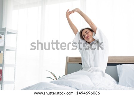 Bright Caucasian woman with stretching after waking up in the morning on the white bed.