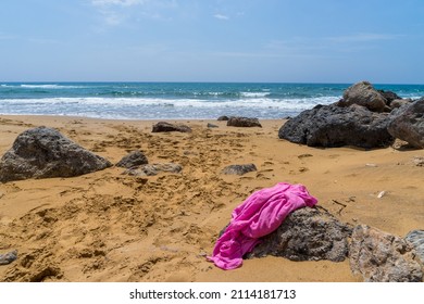 A Bright Cerise Pink Beach Wrap Lies On A Rock On The Beautiful Sandy Shore Of Calblanque, Murcia. Gentle Mediterranean Waves In The Background And Blue Sky With Few Clouds - Copy Space And No People.