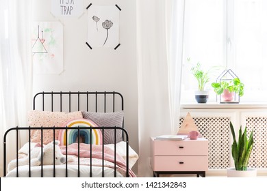 Bright child bedroom with colorful bedding, prints on the wall and pastel pink bedside table, real photo