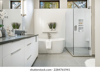 bright clean bathroom with white porcelain glass shower elegant tile grey cabinets basket weave tile on floor with access to laundry and walk in closet - Powered by Shutterstock