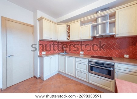 Bright and clean kitchen featuring light wooden cabinets, red tiled splashback, stainless steel fixtures, and a sleek stove design