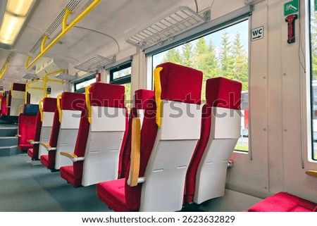 Bright and clean modern train interior showcasing red upholstered seats and large windows offering a scenic view of lush greenery outside. ideal for travel promotion, design inspiration