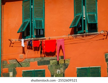 Bright clothing dries on line outside green shuttered windows on orange building creating vivid contrast. - Powered by Shutterstock