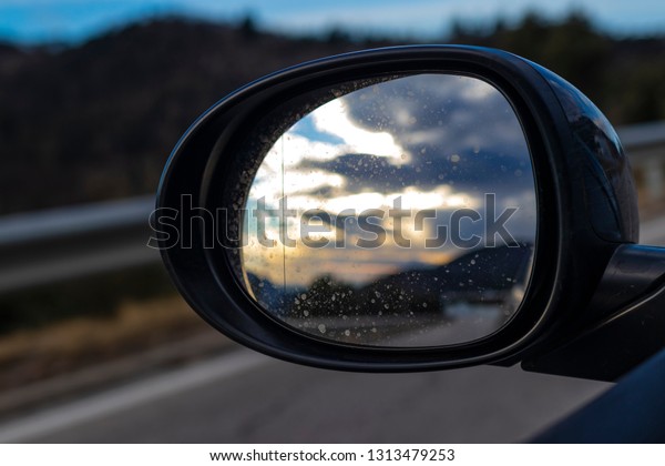 Bright cloudscape reflecting on an oval black\
mirror car while driving on a\
highway