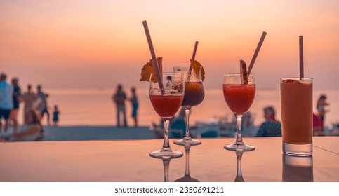 Bright cocktail drinks with blur beach party people and colorful sunset sea sky in background. Luxury outdoor leisure lifestyle, relaxing and romantic colors, blurred people partying on summer evening - Powered by Shutterstock