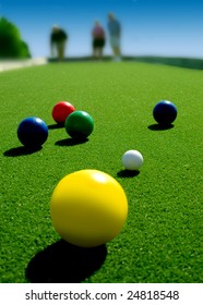 Bright Colored Bocce Balls On Brilliant Green Court. Three Players In Background.