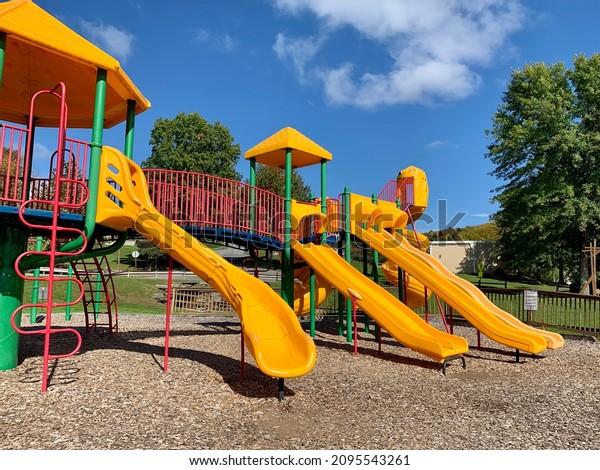 A bright, colorful playground at a\
park. There are obstacle courses, things to climb on, multiple\
slides, a rock wall, and other fun things to play\
on.