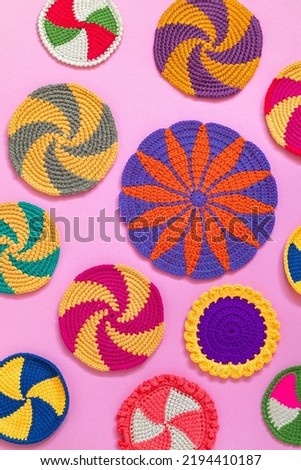 Bright colorful round crochet holders and cup coasters on a pink background. Home craft. Handmade kitchen decor. Top view.