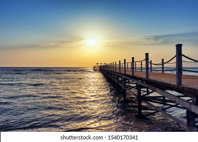 Bright and colorful sunrise over the pier and sea. Perspective view of a wooden pier on the sea at sunrise with rocky islands in the distance - Powered by Shutterstock