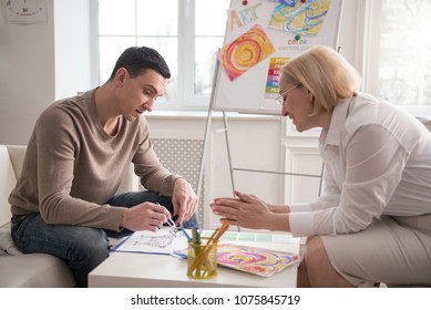 Bright colors. Merry mature psychologist sharing her observation while man drawing - Powered by Shutterstock