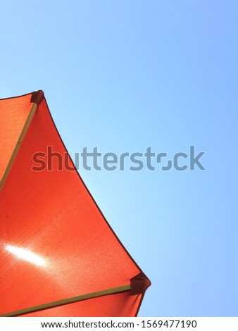 Bright contrast between orange umbrella and vivid blue sky. Optimism and hope. Negative space.