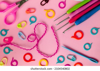 Bright Crochet Tools On A Pink Background. Crochet Hooks, Colored Markers, Needle And Scissors.