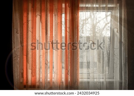Bright curtain is drawn over a window with a trees behind it in the style of dark and light orange retro filters and translucent color with mixed patterns and split toning