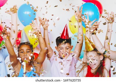 Bright, cute children celebrate a birthday. Multinational party, balloons, confetti, caps, smiles, teenagers are happy raising their hands up.