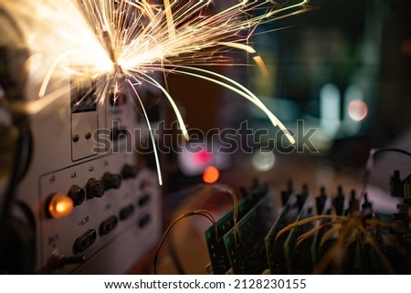 Bright dangerous electronic sparks of current quickly and sharply scatter from an unsafe short circuit on complex technological equipment, in a dark room with electrical appliances
