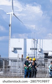 In bright daylight, small distant figures of engineers cross the substation yard between the transformer bays inside the fenced grid substation. Concept of renewable energy, engineering.